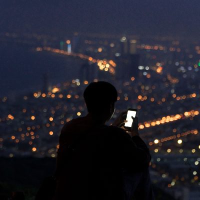 흐릿한 밤거리에 서서 휴대폰 화면을 들여다보는 사람의 뒷모습